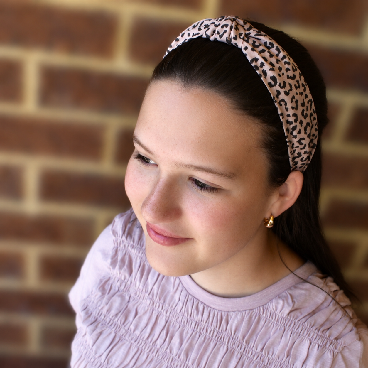 Woman wearing a leopard print headband standing against a brick wall
