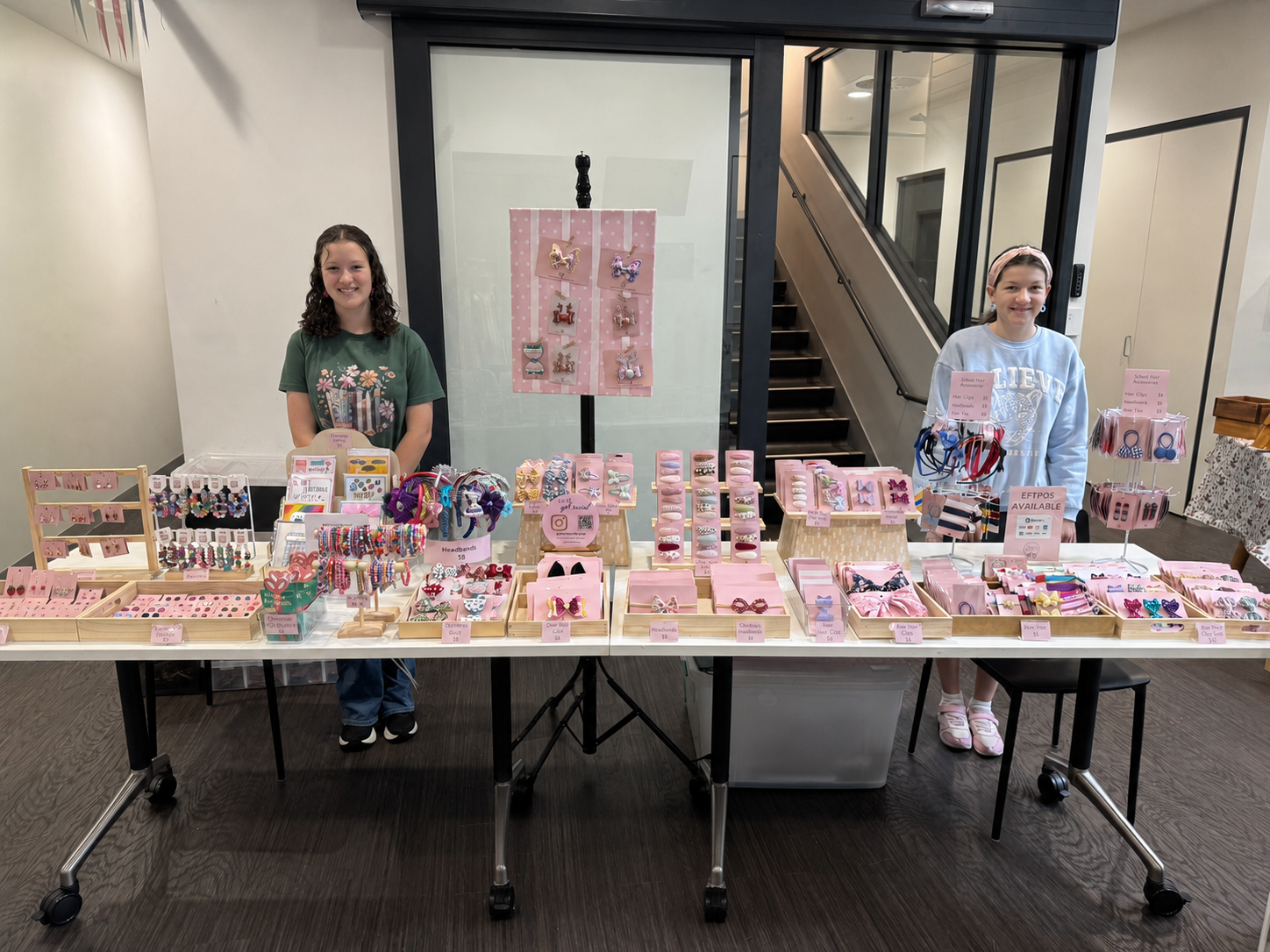 Two daughters of Alice Jean Design's founder, standing behind their market display