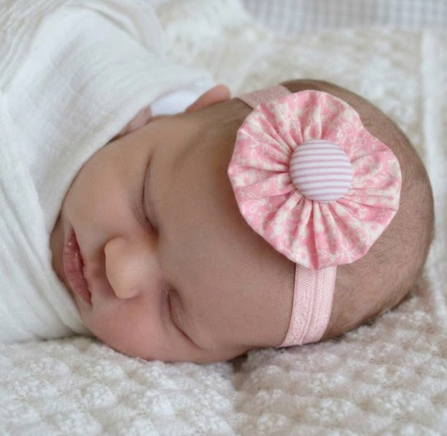 Newborn baby wearing a pink floral headband on a soft white background