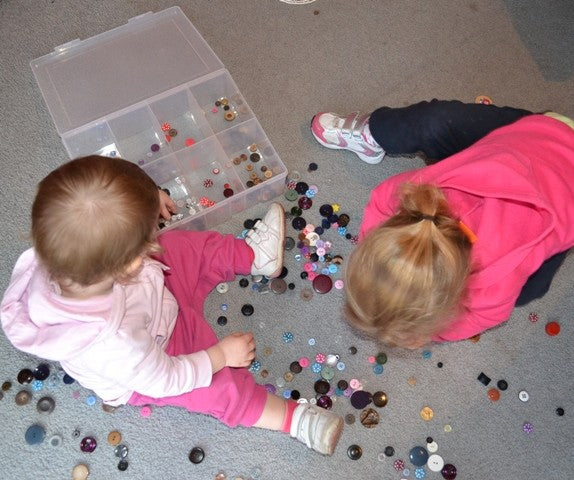 Two children playing with buttons on a carpeted floor.