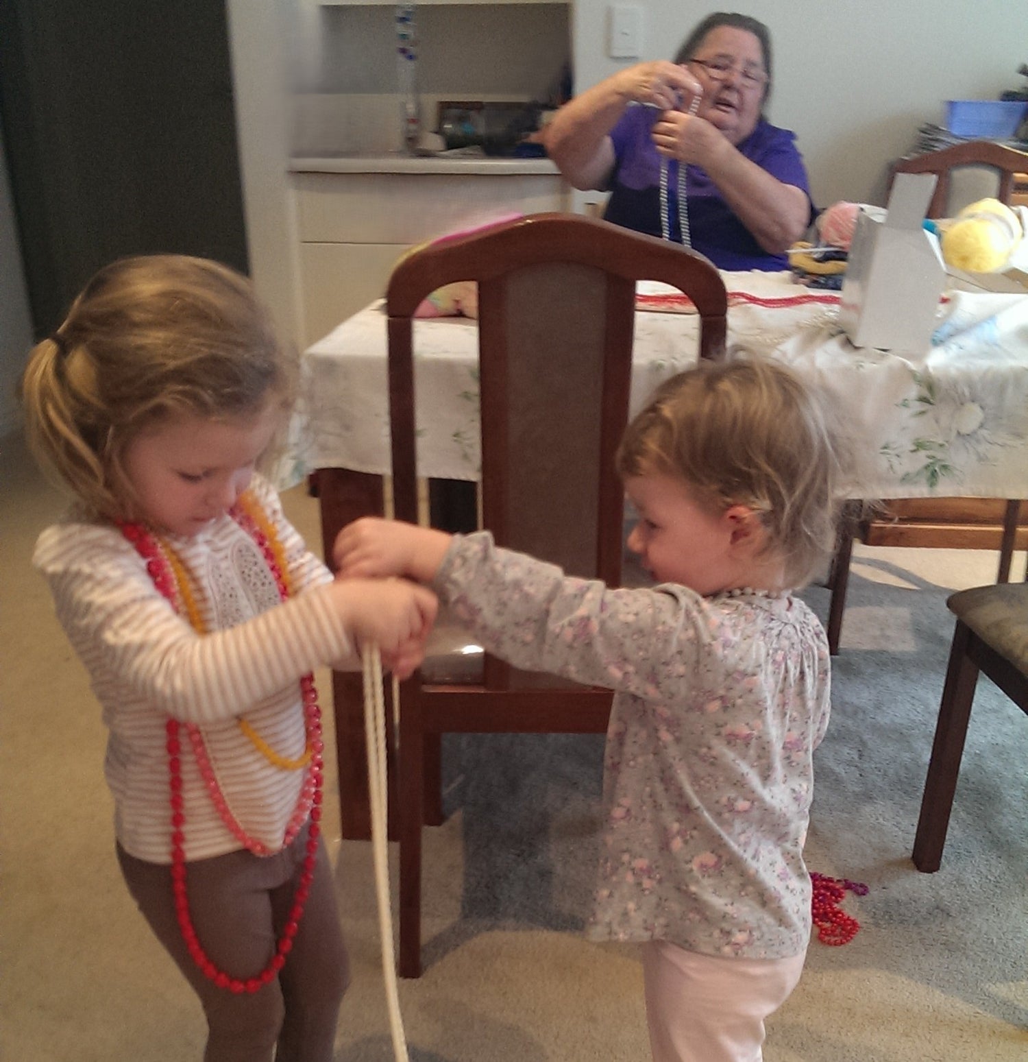 Two young girls playing with beaded necklaces in a home setting.