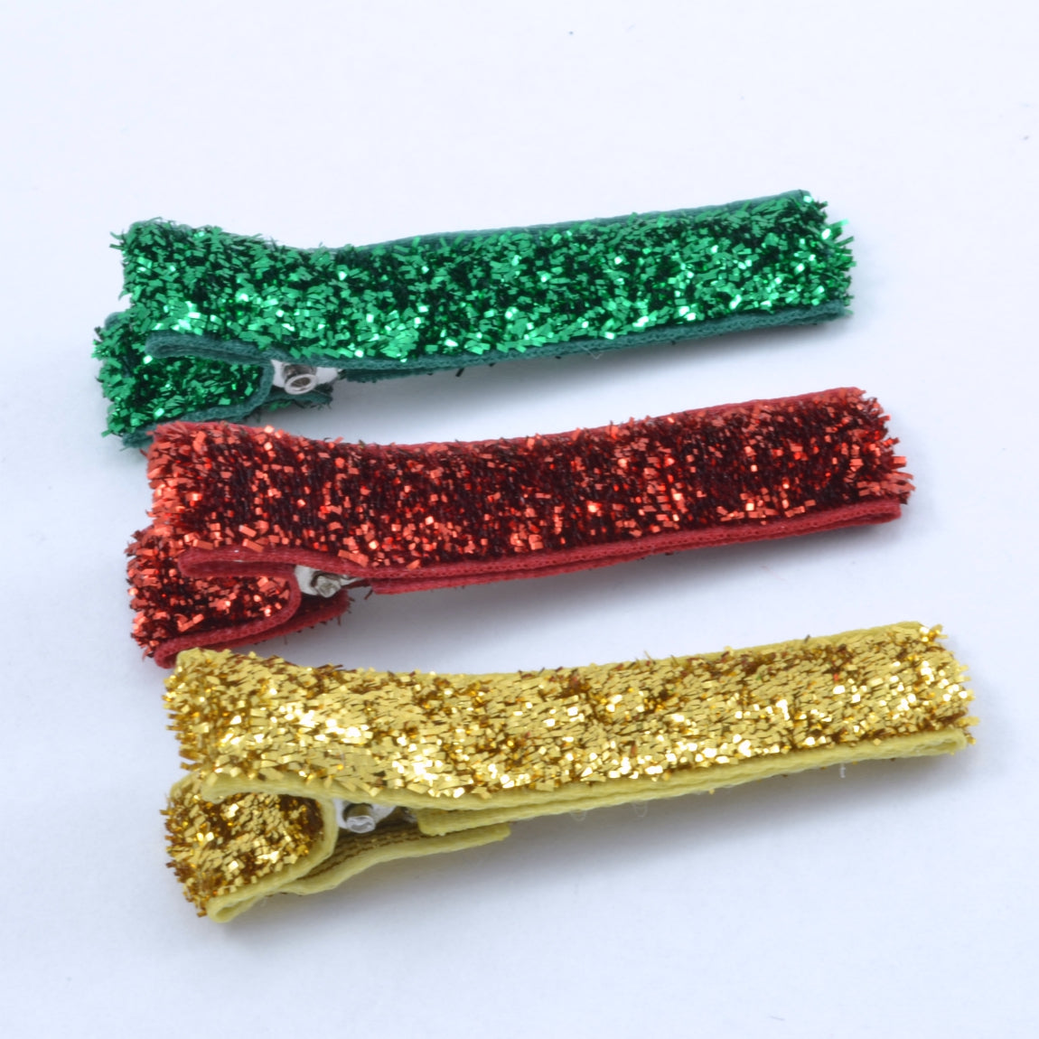 A set of three hair clips with glittery ribbons in red, green, and gold colors.