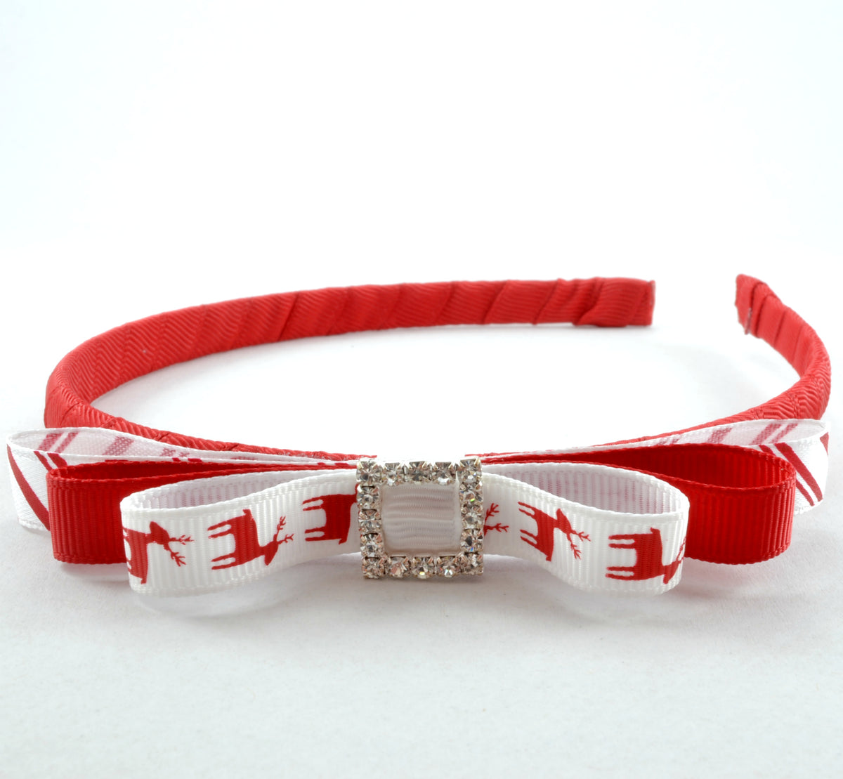 A red and white Christmas-themed headband with a rhinestone buckle in the center, featuring a reindeer design on the white ribbon.
